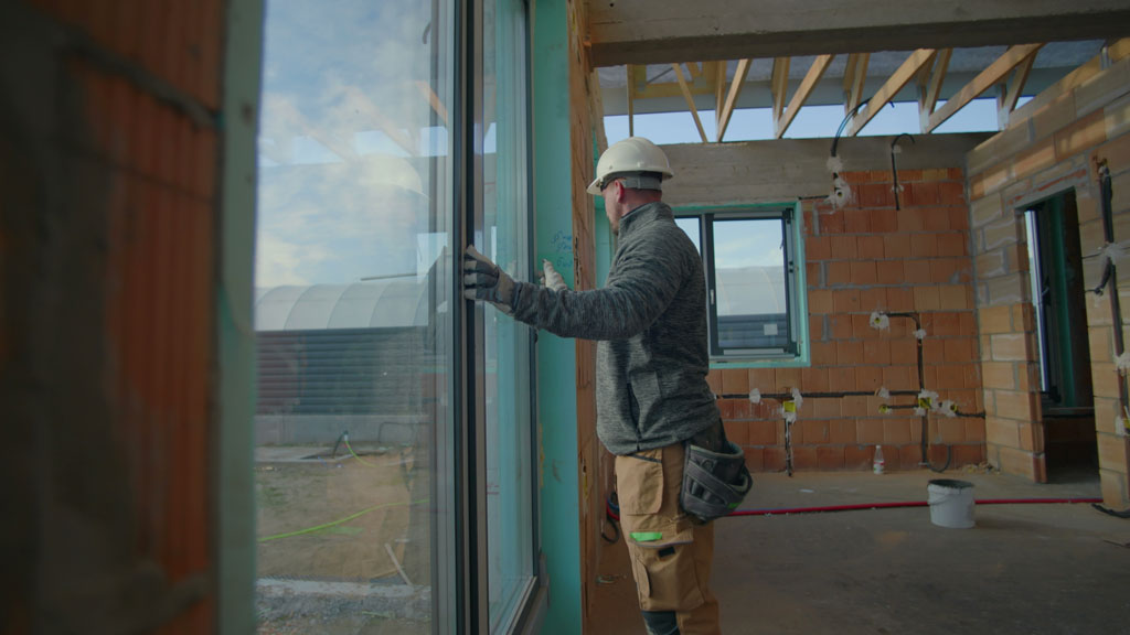 Menuisier vérifiant l'alignement d'une baie vitrée sur extension moderne